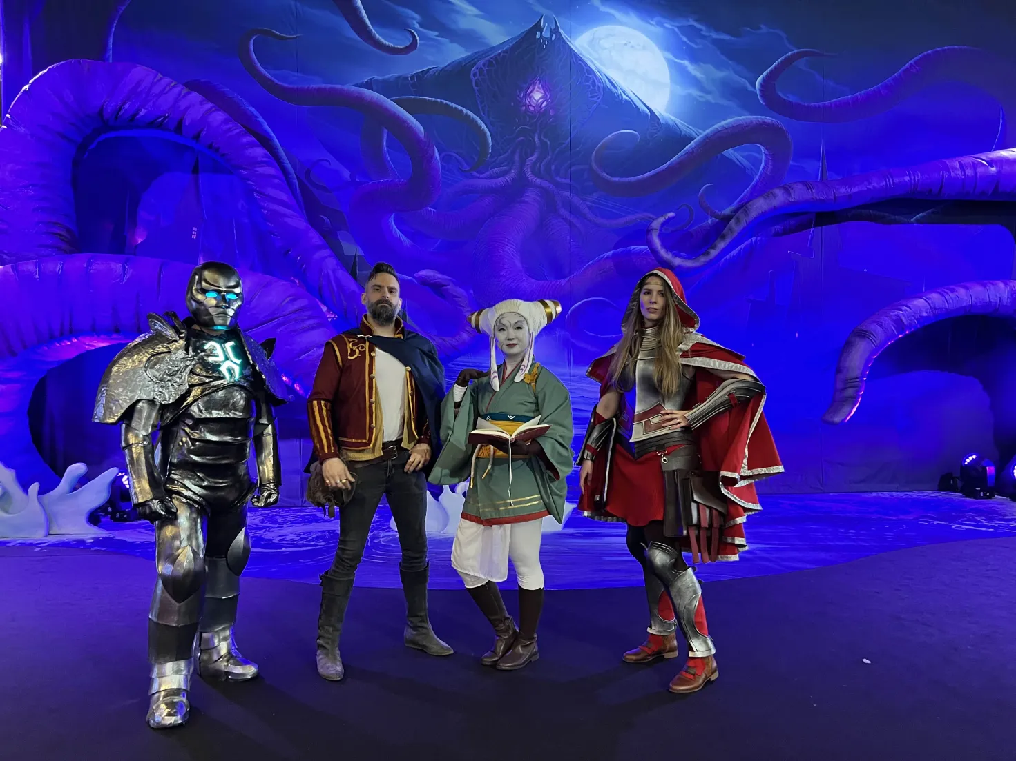 My Karn cosplay lined up with three other cosplayers in front of a giant Eldrazi backdrop.