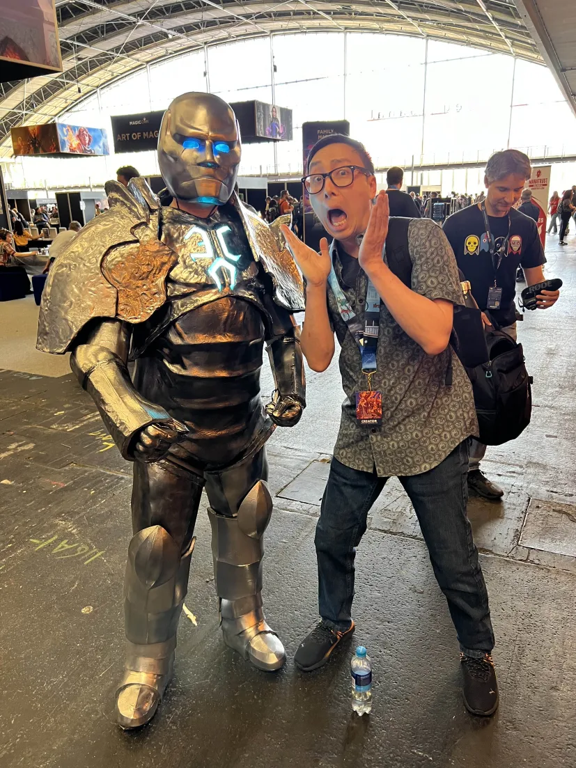 My Karn cosplay next to VeggieWagon pulling a shocked pose under the Art of Magic banner.
